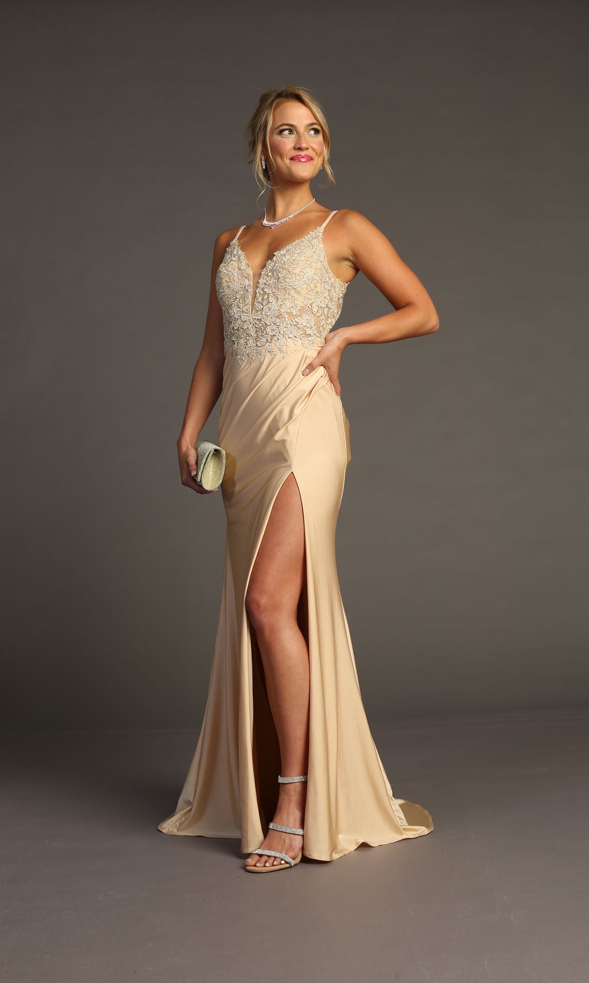 Woman wears the Lace-Bodice Slinky Long Prom Dress (Chicas YG5033), a sleeveless, floor-length gown with a high slit and embroidered lace bodice, holding a clutch against a plain background.